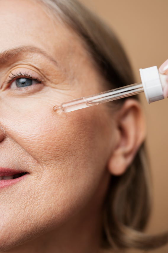 Close-up of a woman applying a dropper of skincare product to her face.
