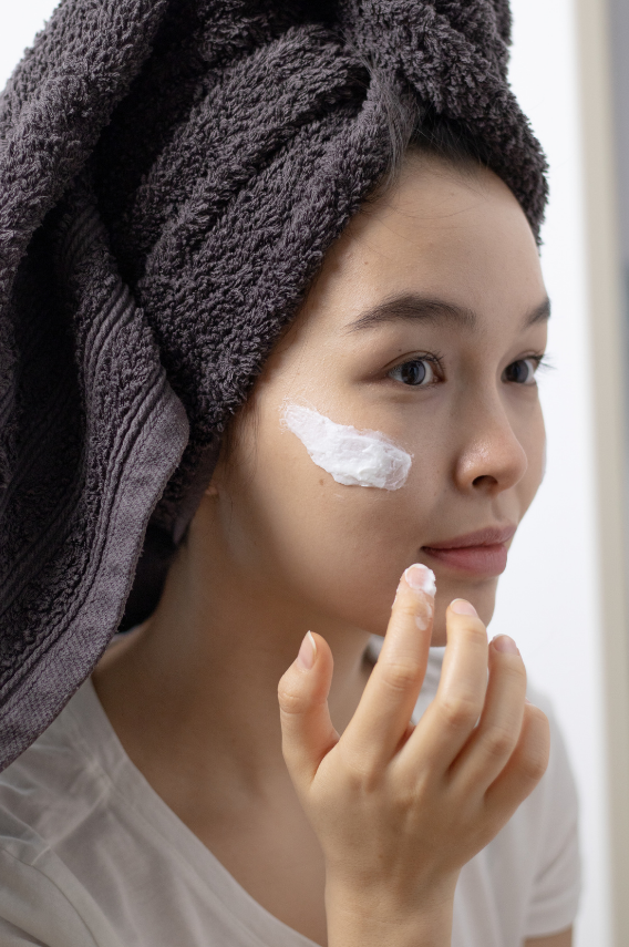 Woman applying cream to her face with a towel on her head.