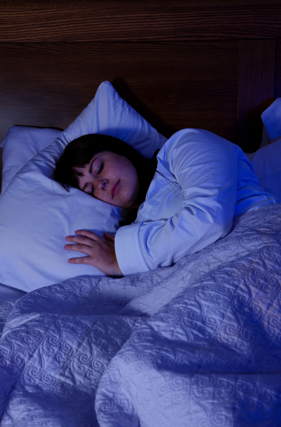 Person lying in bed under a blanket with a dark room setting